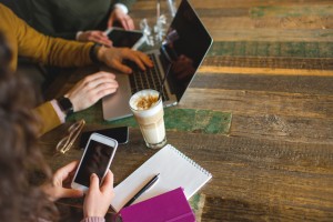 Hands over laptop smartphone and tablet with coffee on the table in trendy cafe